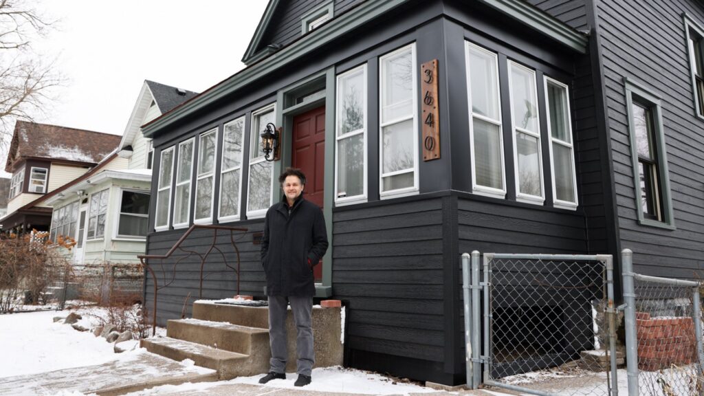 A man standing in front of a house with newly installed dark siding, showcasing work by Archcraft Exteriors in South Saint Paul, MN.