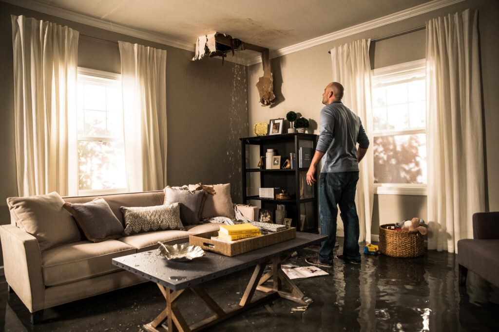 A man inspecting a severe water leak from a damaged ceiling in a living room, handled by ServiceMaster Fire & Water Restoration Services in Lexington, KY.