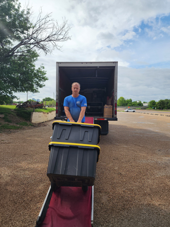 A mover from DFW Moving Company, LLC loading a large bin onto a moving truck in Plano, TX.