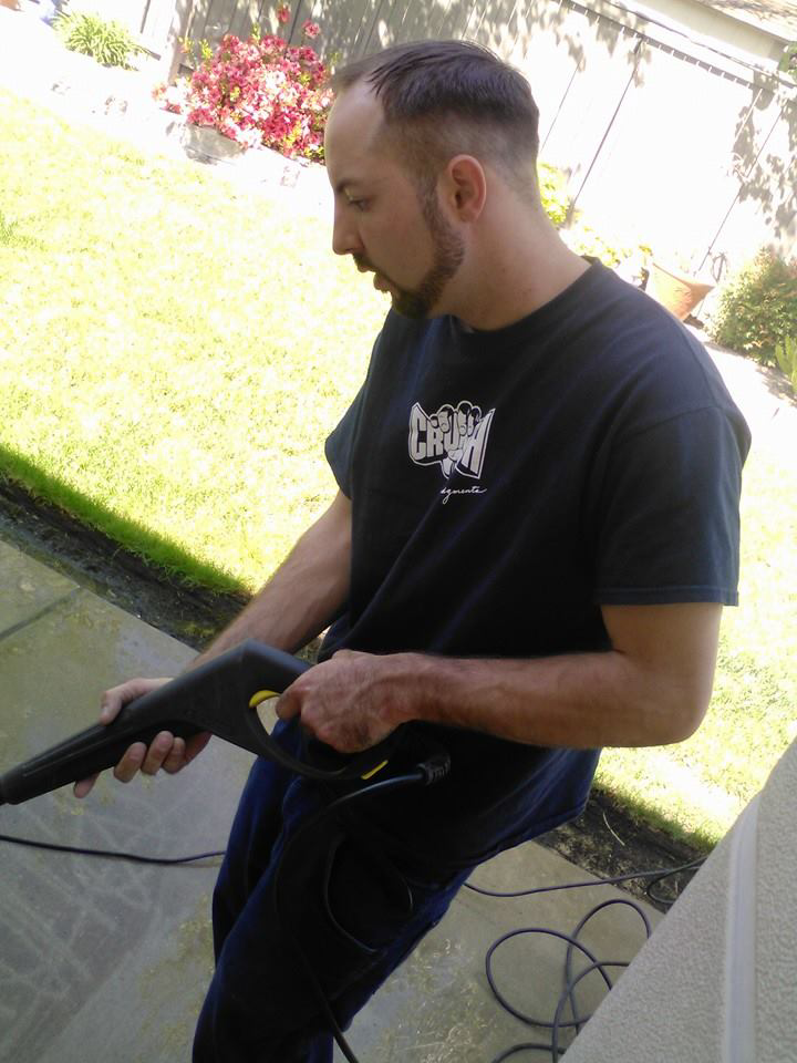 A man from Sister & Brother Cleaning Services pressure washing a residential patio in Sacramento, CA.