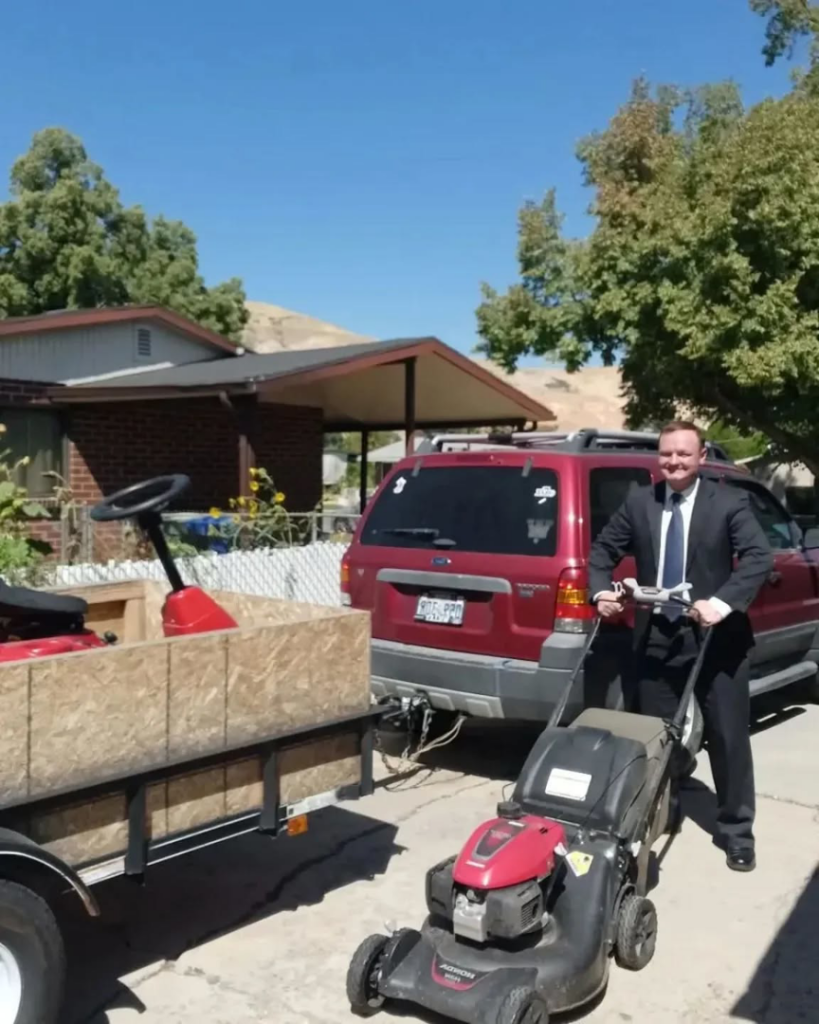 A man pushing a lawnmower, with a trailer carrying additional lawn care equipment for Atkinson Lawn Care Service in Salt Lake City, UT.