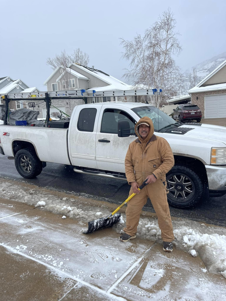 A man shoveling snow from a sidewalk next to a pickup truck, performing snow removal for Medina's Landscape Care LLC in Layton, UT.