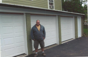 A man standing proudly in front of three newly installed white garage doors by Carriage Overhead in Stamford, CT.