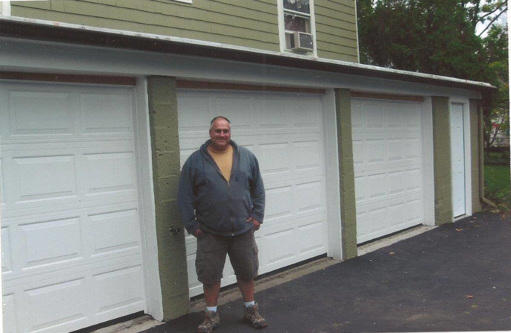 A man standing proudly in front of three newly installed white garage doors by Carriage Overhead in Stamford, CT.