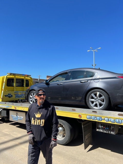 A man standing with a yellow flatbed tow truck from Terry's Auto Service and Towing, LLC, towing a car in Springfield, MO.