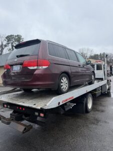 A maroon Honda Odyssey minivan loaded onto a flatbed tow truck from Bullcity Towing & Services LLC in Durham, NC.