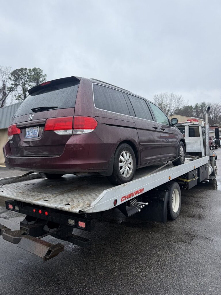 A maroon Honda Odyssey minivan loaded onto a flatbed tow truck from Bullcity Towing & Services LLC in Durham, NC.