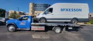 A white McKesson commercial van being transported on a flatbed tow truck by Vatos Locos Towing in Cincinnati, OH.