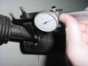 A hand measuring a garage door spring with a caliper for accurate replacement by Sandia Garage Door Repair in Albuquerque, NM