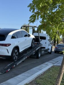 A white Mercedes-Benz EQE SUV being towed by an AJ's Towing Services & Roadside Assistance flatbed truck in Sacramento, CA.