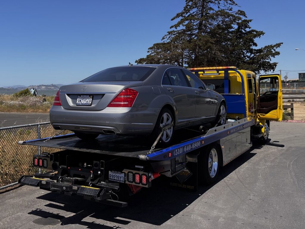 A grey Mercedes sedan is secured on a flatbed tow truck by S&F Towing in Oakland, CA.
