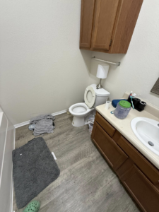 A messy bathroom with clothes on the floor and a dirty toilet, before cleaning by WWJM Cleaning Service in Oklahoma City, OK.
