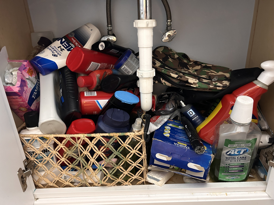 A cluttered bathroom cabinet before professional cleaning and organization by On Course Cleaning in Fayetteville, NC.