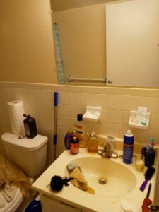 A cluttered and messy bathroom vanity before professional cleaning by Whole New World Cleaning Service, LLC in Wilmington, DE