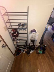 A messy entryway with a shoe rack and items on the floor before professional cleaning by Nannie Needs LLC in Kent, WA.
