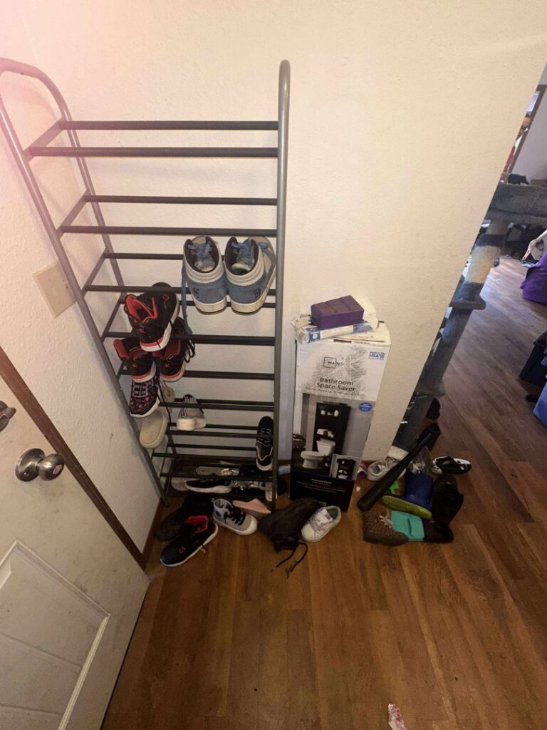 A messy entryway with a shoe rack and items on the floor before professional cleaning by Nannie Needs LLC in Kent, WA.