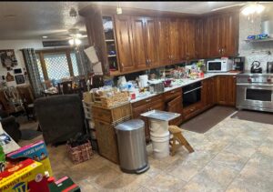 A messy kitchen with cluttered countertops and a dirty floor before house cleaning by Teri Lynn's Cleaning in Williston, ND.