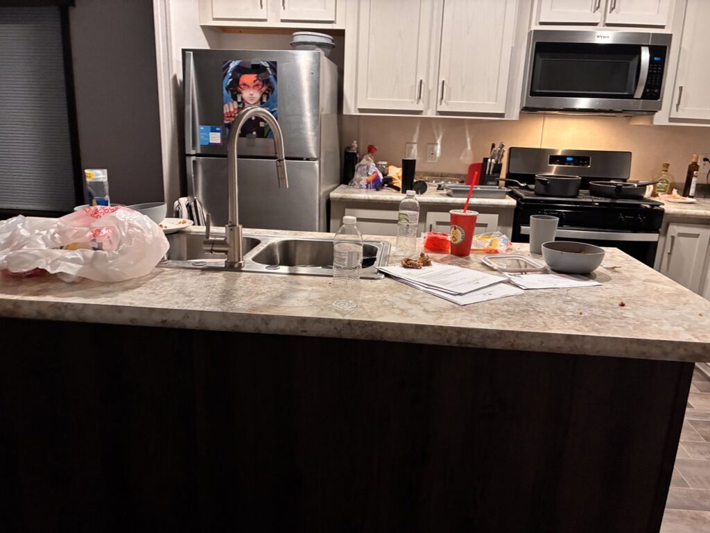 A messy kitchen island with dishes and clutter, showing a 'before' scene for Heavenly Harlots Maid Cleaning Services in Grand Forks, ND.