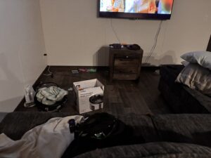 A messy living room floor with various items and boxes, a 'before' scene for Heavenly Harlots Maid Cleaning Services in Grand Forks, ND.
