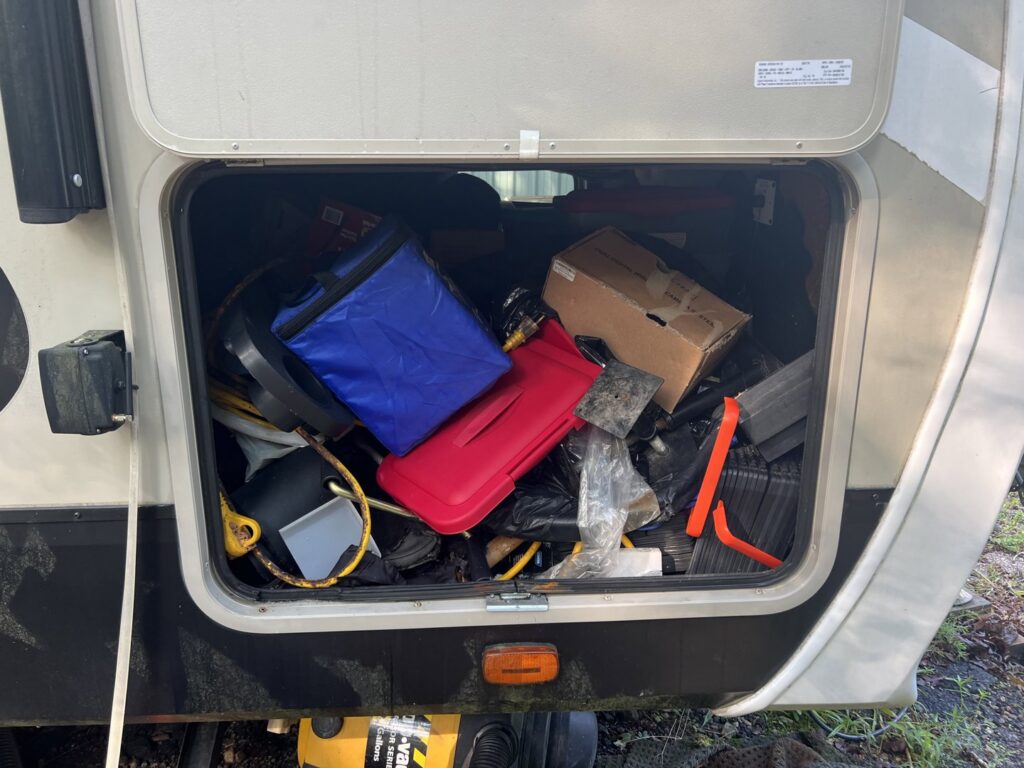 A cluttered and messy RV storage compartment, showing a 'before' state for cleaning and organization by SetApart Home Concierge in Greenville, SC.