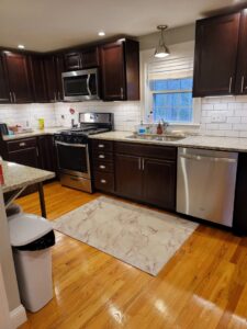 A meticulously cleaned kitchen featuring dark cabinets, stainless steel appliances, and hardwood floors by Cate's Cleaning Company in Derry, NH.