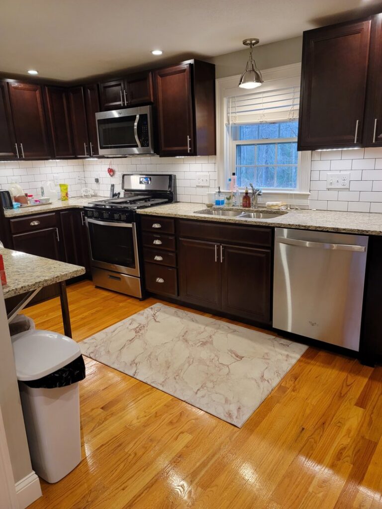 A meticulously cleaned kitchen featuring dark cabinets, stainless steel appliances, and hardwood floors by Cate's Cleaning Company in Derry, NH.