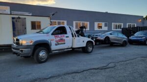 A Milan Towing inc. truck towing two cars, one on the flatbed and one behind, in Milan, MI.