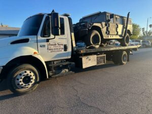 A military-style Humvee being transported on a flatbed tow truck by Crisanto Towing in Phoenix, AZ.