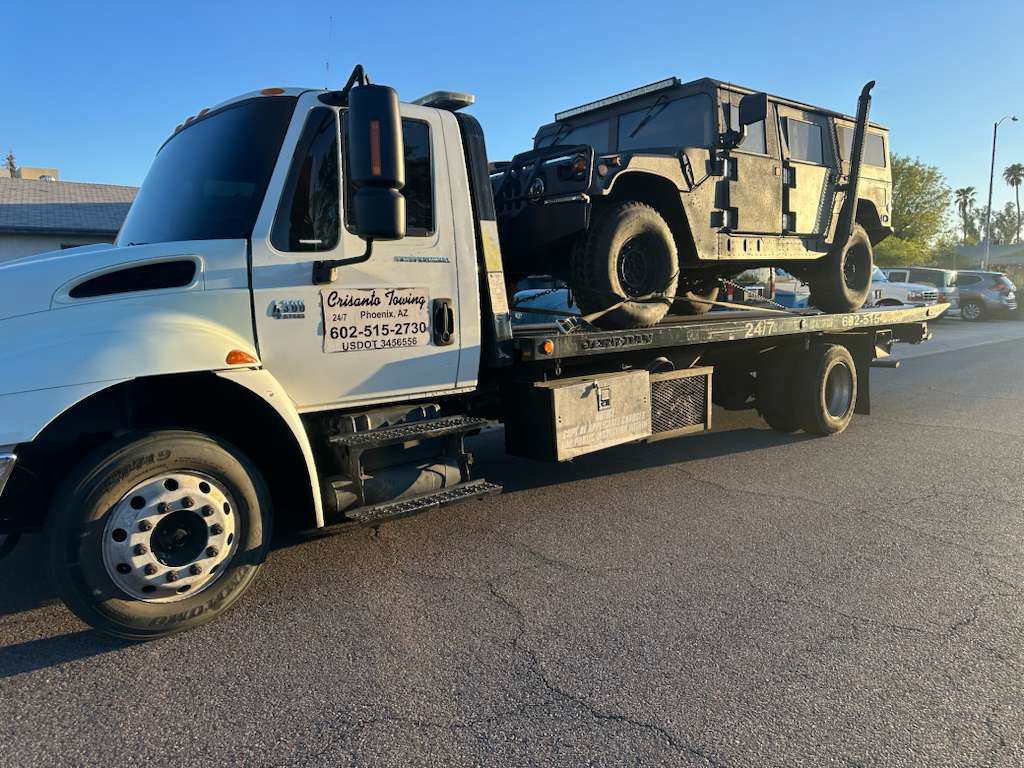 A military-style Humvee being transported on a flatbed tow truck by Crisanto Towing in Phoenix, AZ.