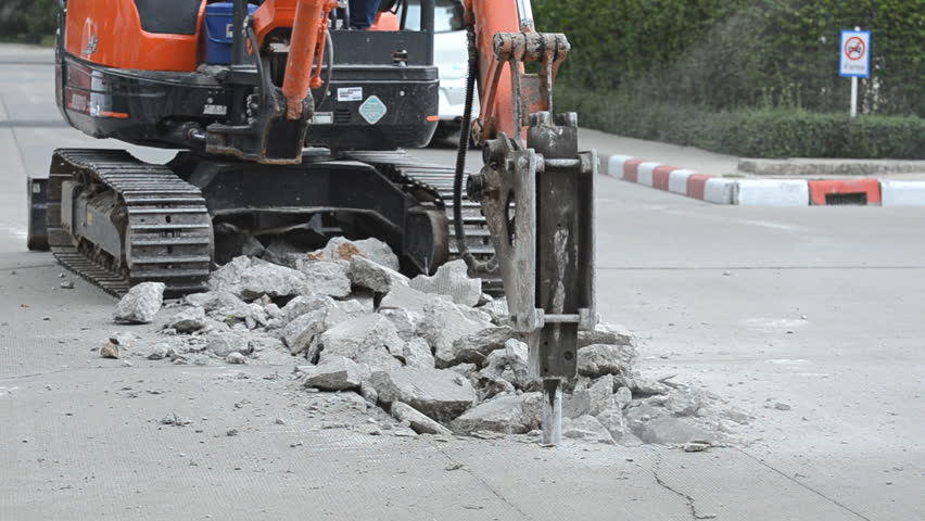 A mini-excavator with a hydraulic breaker attachment demolishing concrete on a road, a service by Torrado Demolition in Houston, TX.