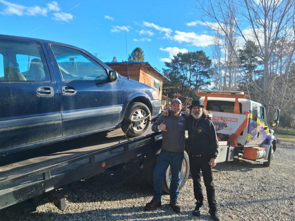 Two men standing next to a minivan being loaded onto a flatbed tow truck by Idaho State Towing and Recovery in Caldwell, ID.