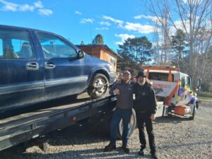 Two men standing next to a minivan being loaded onto a flatbed tow truck by Idaho State Towing and Recovery in Caldwell, ID.