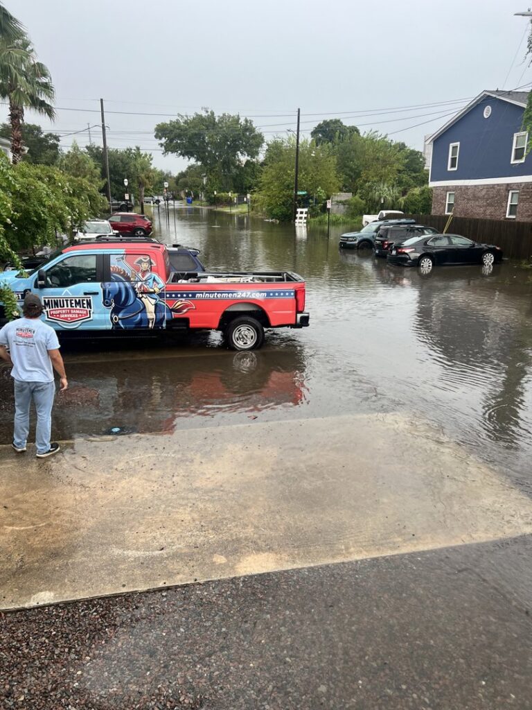 A Minutemen Property Damage Services truck parked on a flooded street with a worker, responding to water damage in North Charleston, SC.