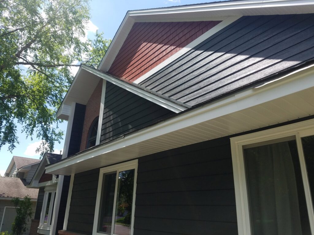 An exterior view of a house showcasing dark gray horizontal and red shake siding with brick by Triton Exteriors in Maple Grove, MN.