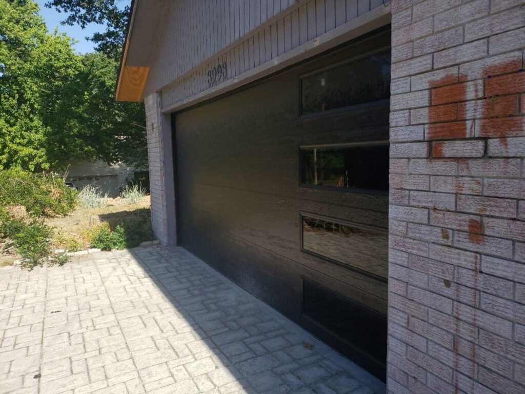 Modern black garage door installed on a brick house by Garage Doors & More in Bentonville, AR