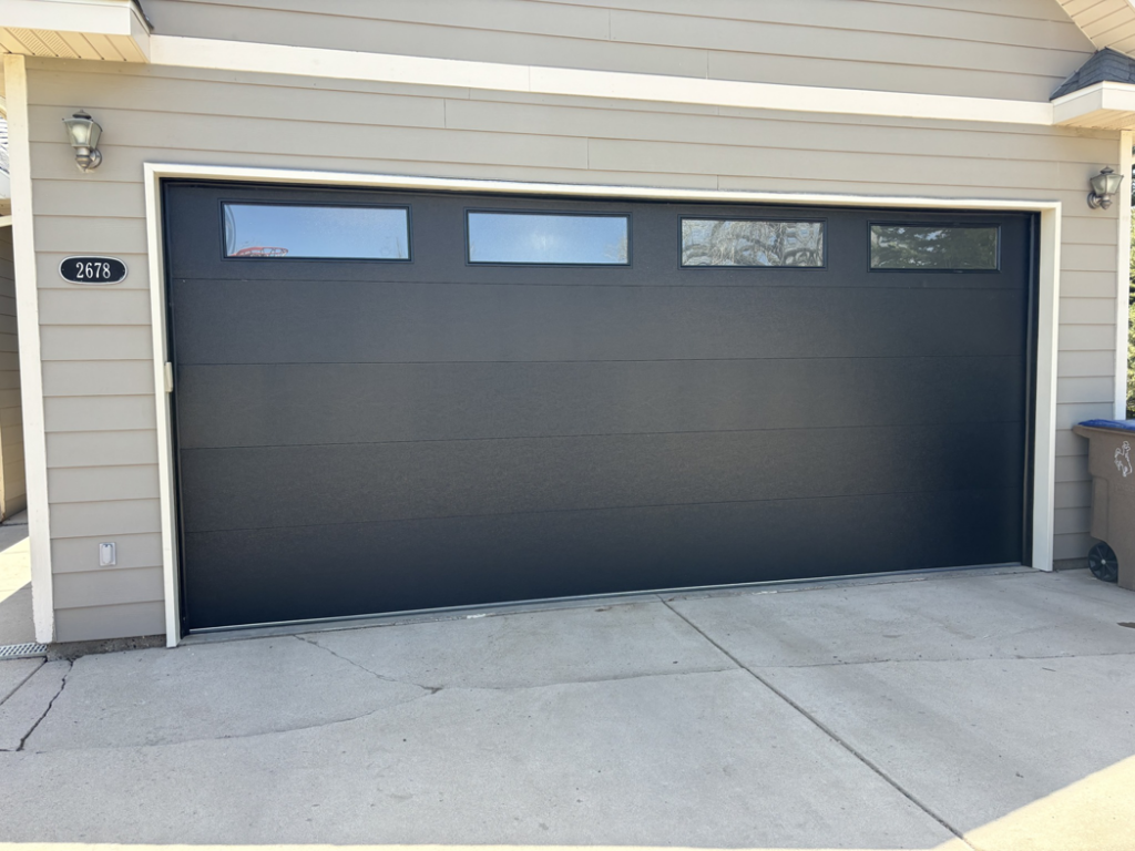 A newly installed modern black garage door with horizontal windows on a residential home by Laramie Garage Doors in Laramie, WY.