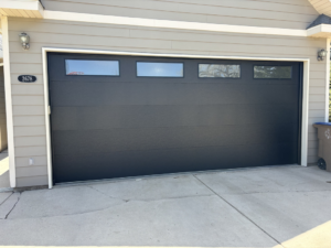 A newly installed modern black garage door with horizontal windows on a residential home by Laramie Garage Doors in Laramie, WY.