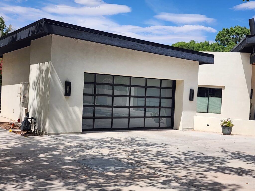 A modern house featuring a large black garage door with multiple windows, installed by Quality-Brand Garage Doors in Rio Rancho, NM.