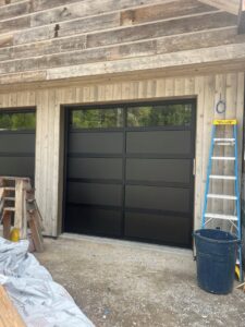 A modern black garage door with windows at a construction site, installed by Riverside Garage Doors in Kalispell, MT.