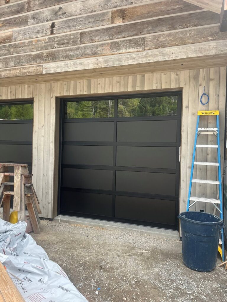 A modern black garage door with windows at a construction site, installed by Riverside Garage Doors in Kalispell, MT.