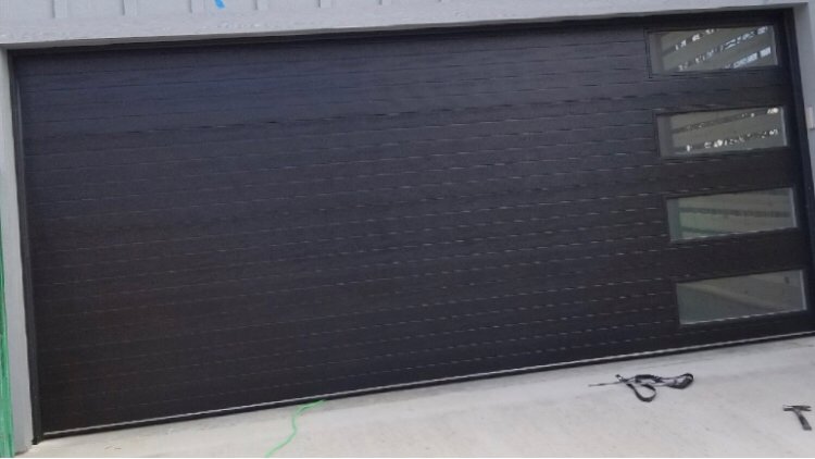 A sleek modern black garage door with horizontal panels and windows by Action Garage Door in Jacksonville, AR.