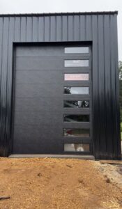 A modern black garage door with multiple windows installed on a black metal building by LaFrancis Overhead Door LLC in Little Rock, AR