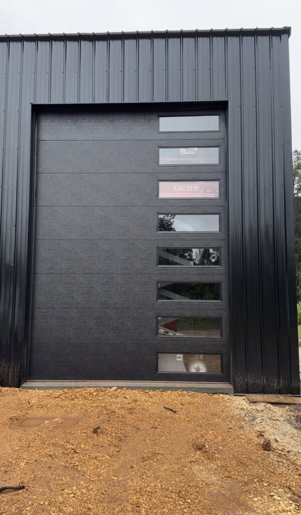 A modern black garage door with multiple windows installed on a black metal building by LaFrancis Overhead Door LLC in Little Rock, AR