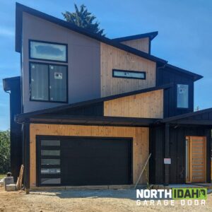 A modern black garage door with frosted windows installed on a newly built contemporary home by North Idaho Garage Door in Coeur d'Alene, ID.