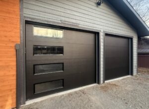 Two modern black garage doors with windows installed on a residential property by Elite Doors in Wasilla, AK.