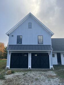 Two modern black garage doors with cross-buck design on a light blue residential home, installed by RidgeLine Overhead Garage Door of CT in Danbury, CT