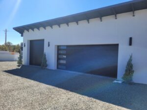 Two modern black garage doors with frosted glass panels installed on a white stucco building by Precision Garage Door of Albuquerque and Santa Fe, NM.