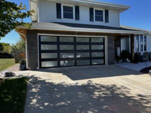 A modern black full-view glass garage door on the exterior of a home, installed by Over The Top Garage in Albuquerque, NM.