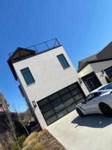 A modern black glass garage door installed on a white brick house by Garage Door Sales & Repair in Conway, AR.