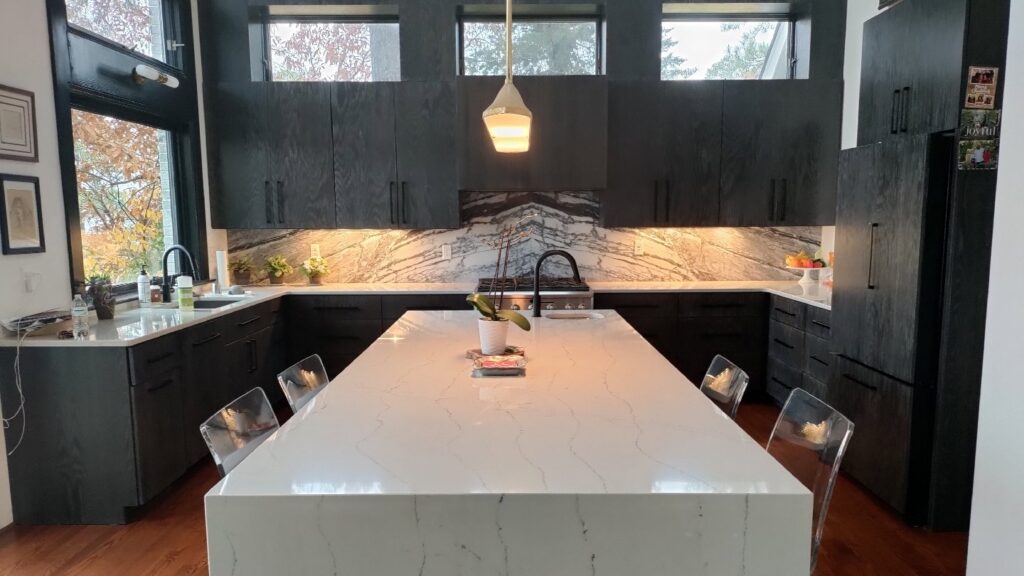 A modern, clean kitchen with dark cabinets, a large white island, and pendant lighting, cleaned by Tessa's Cleaning Service in Chesapeake, VA.